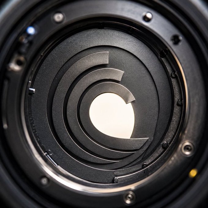 A close-up view looking into the circular lens and aperture blades of a black camera lens.