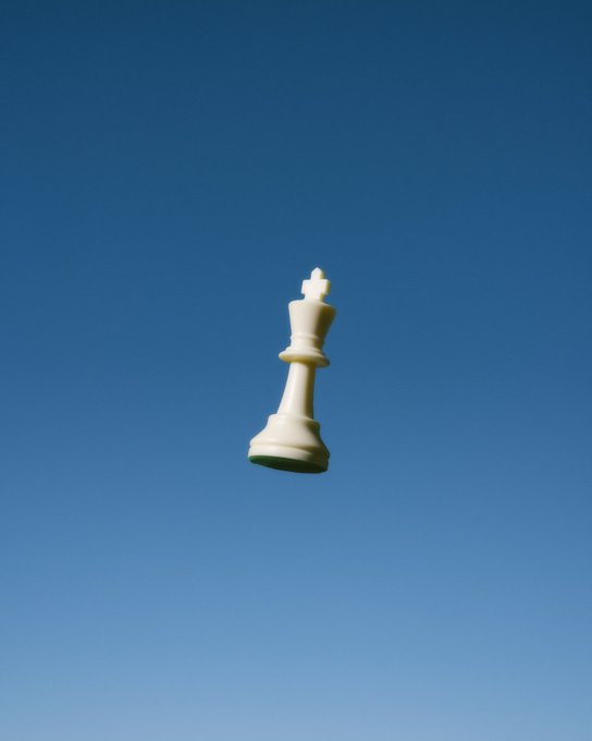 An artistic photograph of a large white chess king piece appearing to float against a clear blue sky gradient.