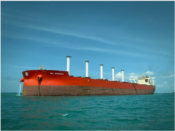 A large red and white bulk carrier ship with multiple cargo cranes, named 'SEA ZHONGHAI', anchored in blue ocean waters under a partly cloudy sky.