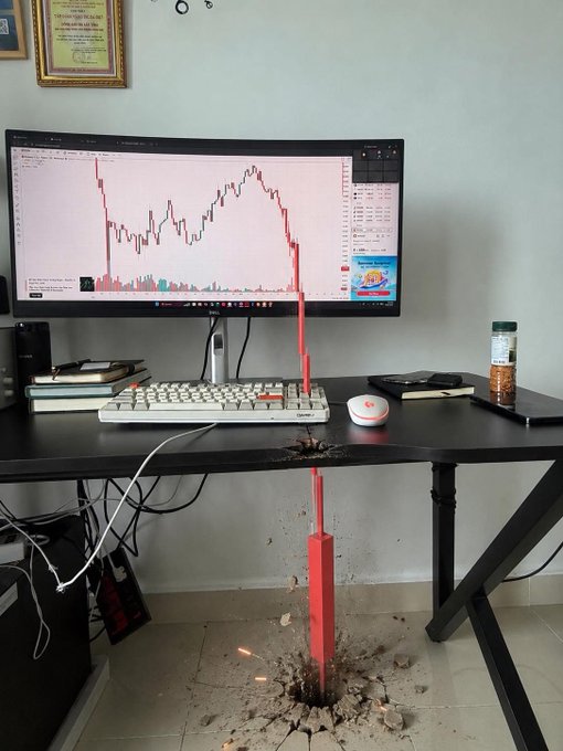 The image shows a computer desk with various items on top, including a keyboard, mouse, and books. The monitor of the computer displays an interesting graph or chart that has caused some damage to the floor beneath. This unusual situation might be related to market trends, stock prices, or financial news, which has led to this peculiar event in the room.