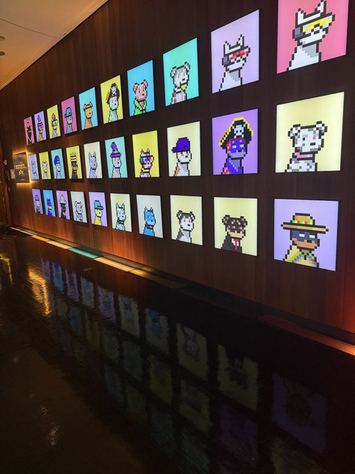 An art installation displaying a grid of illuminated pixel-art portraits of various characters in bright, colorful frames mounted on a dark wood-paneled wall.