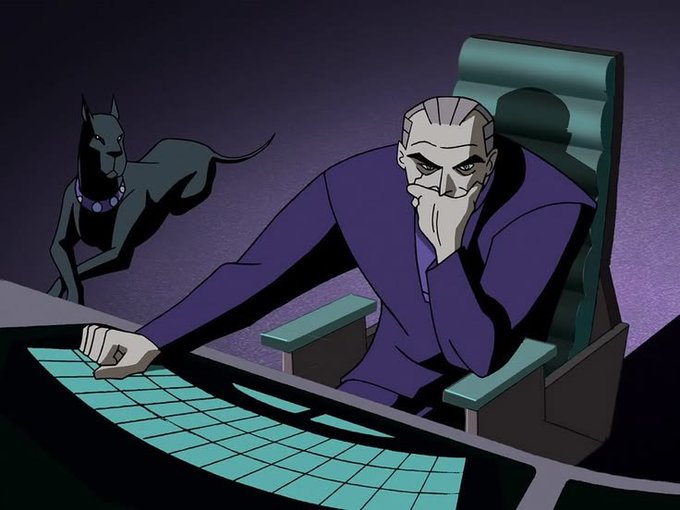 An animated scene showing a gaunt, pale man in a purple coat sitting at a glowing computer console with a black dog behind him, appearing to be from a Batman: The Animated Series episode.