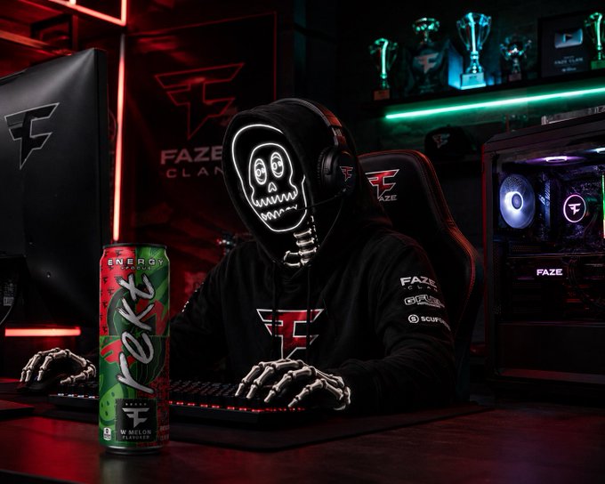 A FaZe Clan esports setup featuring a skeleton mascot in a black hoodie wearing a glowing LED skull mask, sitting at a gaming PC with skeleton hands on the keyboard, alongside a Henergy watermelon-flavored energy drink can.