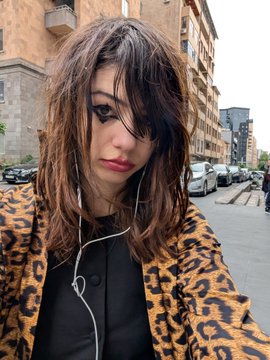 The image features a woman with long brown hair wearing a leopard print jacket, listening to music through earbuds while looking at the camera. She has her hand on her face as if posing for a photo or video. The caption "Going live on duel" suggests that she is participating in an event where people share their experiences and moments online, possibly related to a specific cause or theme.