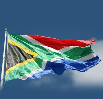 The South African flag waves against a blue sky, visually representing the nation that is proposing new rules for offshore crypto transfers, requiring licensed platforms and reporting to the central bank.