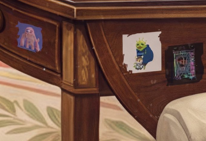 A wooden desk drawer displays three small stickers featuring cartoon characters—a pink ghost, a green crowned figure, and a dark character—representing the "just_t00ns" NFT collection that has reportedly caught Beeple's attention, with 333 NFTs burned and 260 ETH in total volume.
