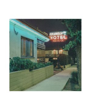 A nighttime photograph of the 'Hollywood Drift-Inn Motel' neon sign glowing red above a two-story building next to a sidewalk.