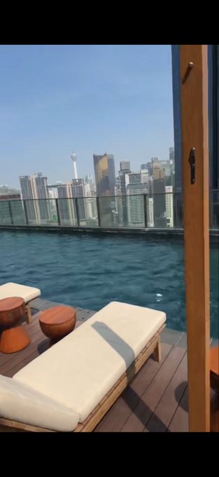 A luxurious infinity pool overlooks a city skyline with a prominent observation tower, suggesting the chartered flight destination mentioned in the post. The upscale setting reflects the exclusive nature of the "OKX chartered flight" experience referenced in the message.
