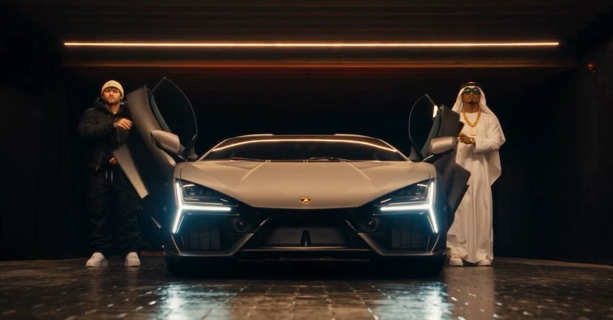 Two men pose on either side of a matte-gray Lamborghini with its scissor doors open in a dimly lit garage—one in dark streetwear and a beanie, the other in a white thobe and gold chain—appearing to celebrate the giveaway winner's whitelist spot mentioned in the caption.
