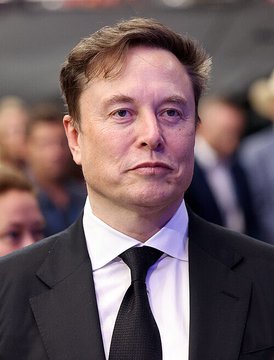 The image shows a man dressed in a suit, wearing a tie, standing against a gray background with several other people present behind him. The main subject of the photo appears to be focused on by the viewer, who seems to be looking at the man or something else in front of them.

In the post accompanying this image, there is a claim that suggests the man might be considering suing Ro Khanna for his involvement with DOGE (Drug Abuse Detection Olfactory Explosivle). The post also mentions that Khanna has been lying about her responsibility to the children. This adds an element of intrigue and potential legal action to the scene depicted in the image, as it seems to be connected to a controversial or potentially harmful situation involving Ro Khanna.