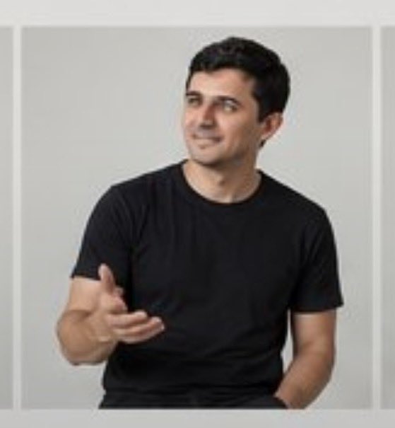 A man with dark hair wearing a black t-shirt gestures with his hand while looking off to the side.