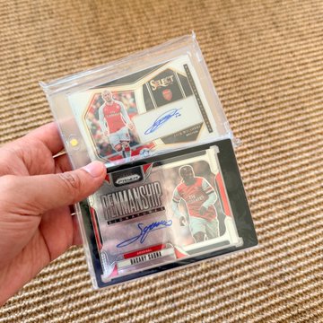 A hand holds two encased autographed hockey trading cards, including one labeled "DOMINIK HASEK" for Buffalo Sabre, displayed in front of a textured beige background.