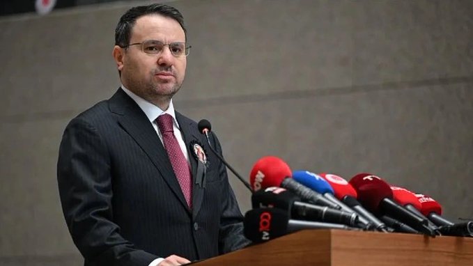 A man in a dark suit and burgundy tie stands at a podium surrounded by multiple microphones from various Turkish news outlets, including ones marked with "8" and "NTV." The image accompanies a breaking news statement attributed to Akın Gürlek regarding SPK and MKK actions against individuals suspected of manipulative financial activities, with assets frozen and five people returning funds to TMSF.