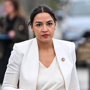A woman with dark hair pulled back, wearing a white blazer and red lipstick, stands outdoors with a serious expression, accessorized with a pin on her lapel. The image appears to relate to the post's claim about Alexandria Ocasio-Cortez (AOC) reportedly dating Vitalik Buterin, though no text or identifying details are visible in the photo itself.