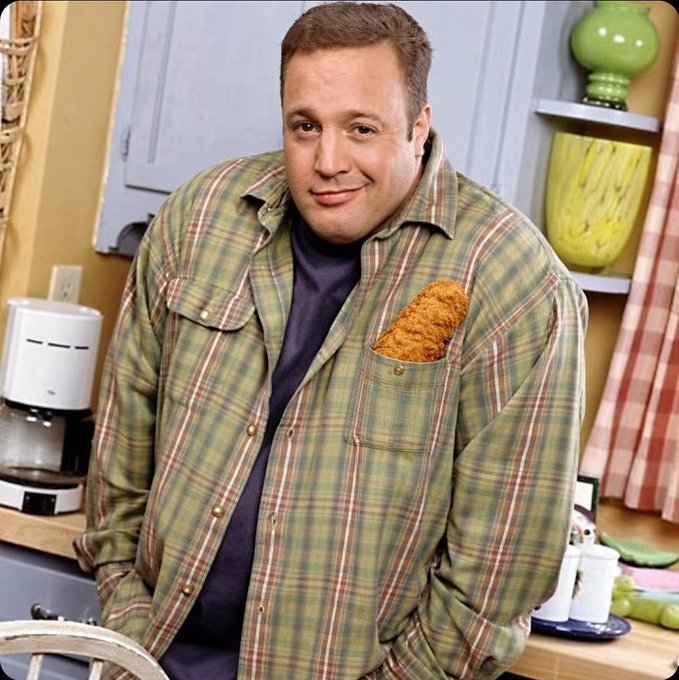 Kevin James stands in a kitchen setting wearing a green plaid flannel shirt over a purple t-shirt, with a piece of fried chicken comically tucked into his chest pocket.