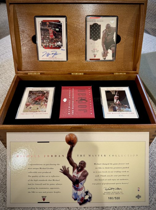 The image features a wooden box containing three basketball cards, including one of Michael Jordan. The box has a brown color and is placed on top of a white surface. The cards are neatly arranged inside the box, showcasing their value as collectibles.