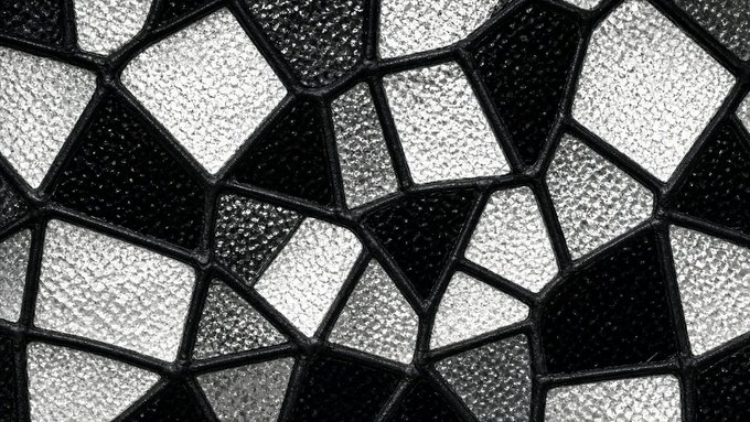 Close-up of a textured black and white geometric mesh or screen pattern with irregular diamond-shaped openings.