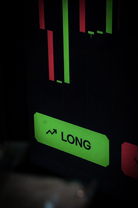 A bright green "LONG" button with an upward trending arrow icon is highlighted on a trading screen, emphasizing a bullish position, while red bearish bars are visible in the background—capturing the perpetual futures (perps) trading action promoted at the Solflare booth at Solana Summit Serbia.