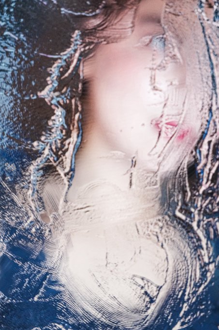 An abstract, distorted image with blue, white, and pink colors that appears to show a figure obscured by rippled, liquid-like textures.