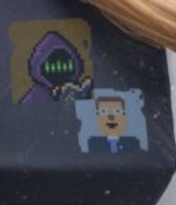 A pixel art image showing two characters against a dark starry background, featuring a hooded purple-robed figure with glowing green eyes and a man in a suit with a surprised expression on a white pillow.