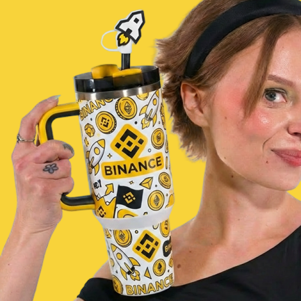 A woman wearing a black headband holds up a large white and yellow travel mug decorated with crypto-themed icons and the word 'BINANCE', set against a bright yellow background.