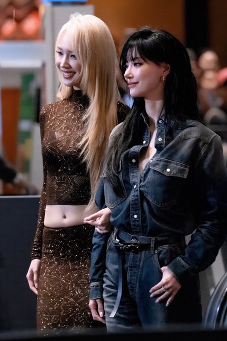 Two young women pose together at an event, with the one on the right—dressed in a dark denim shirt and pants, matching the post's focus on "jingjing yu"—wearing a sharp, handsome look while her blonde companion in a brown sparkly two-piece outfit stands beside her. The styled poses and formal event backdrop align with the fan caption celebrating Jingjing Yu's appearance at the M Choice Mint Awards 2026.