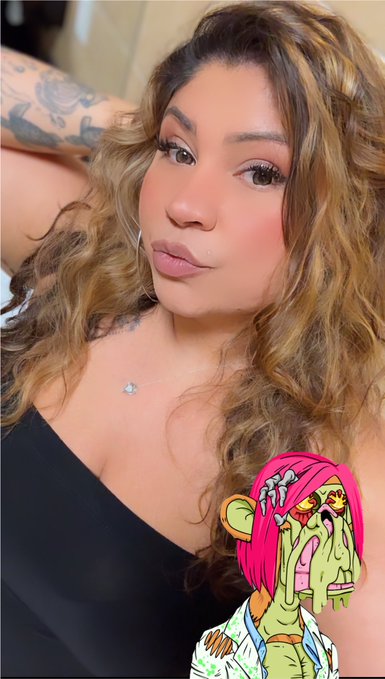 A young woman with long, wavy highlighted hair poses in a black top, flashing her toned arm tattoos while a snotty, pink-haired zombie Mutant Ape cartoon graphic overlays the corner—tying into her cheerful "Happy Mutant Monday Apes" post celebrating a busy day well-spent.