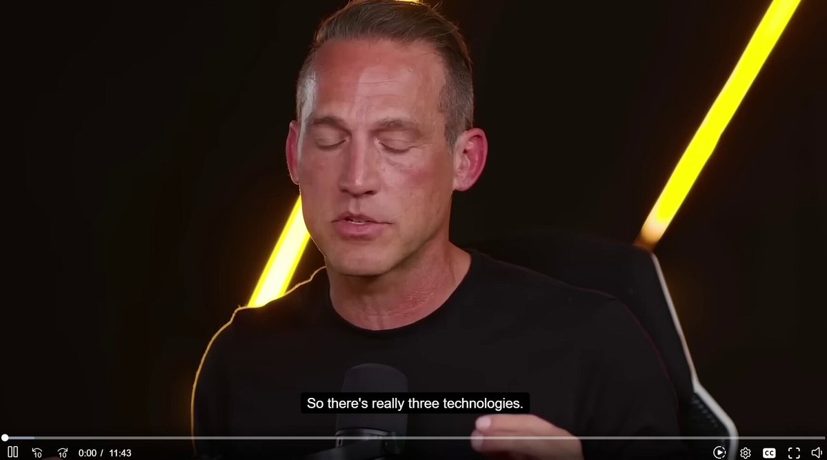 The image shows a man wearing a black shirt, sitting down with his hands together as if he's deep in thought or contemplation. The background of the image is dark, which contrasts with the bright yellow lines behind him. There are also some words written on the screen that read "So's there really three technologies". This phrase seems to be related to the man and the technology being discussed in the image.
