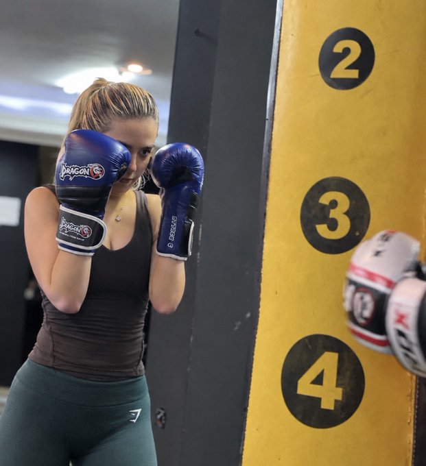 A woman wearing blue boxing gloves labeled 'DRAGON' poses in a fighting stance next to a yellow wall section marked with the numbers 2, 3, and 4 in black circles.