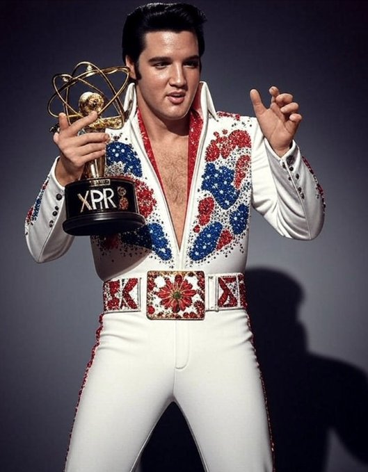 In the image, a man dressed as Elvis Presley is holding a trophy with both hands. The trophy has a gold base and a blue and red design that resembles the iconic suit worn by the famous singer. The text "The King Is Coming Proton is the chosen one!" is also present in the image. This suggests that the man might be participating in an event or celebration related to Elvis Presley, such as a tribute or a special edition of his music.