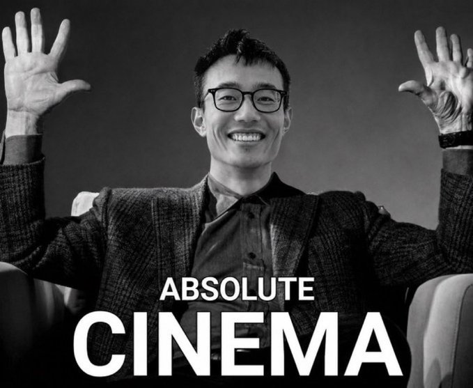 A black-and-white photo of a smiling man with glasses raising both hands excitedly, overlaid with the text 'ABSOLUTE CINEMA'.