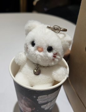 A small white fluffy bear plush toy with a metal clip and chain attached, sitting inside a decorative container.