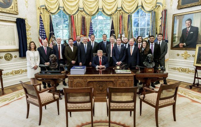 President Donald Trump sits at the Resolute Desk in the Oval Office surrounded by a group of approximately 20 officials and aides, with the portrait of George H.W. Bush visible on the right wall.

The image shows the Trump administration in a formal White House setting, which the post uses to emphasize a political point about directional shifts, while the $XRP ticker references the cryptocurrency market.