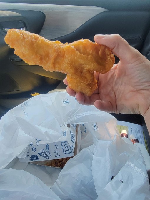 A hand holds up a large, golden-brown fried fish stick in front of a car's interior, with an open plastic bag revealing a Long John Silver's box (marked "order #169") below. Caption: "SMASH — when the fish stick is so comically oversized it looks like it belongs on a sword, you eat it and ask questions later."