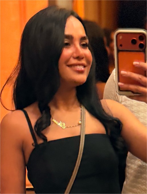 A woman with long dark hair wearing a black top and a name necklace takes a mirror selfie with her iPhone, smiling brightly. The post's upbeat morning greeting and reference to "$KAITO" being "on fire" mirrors her cheerful, ready-to-go vibe, signaling excitement for the trading day ahead.