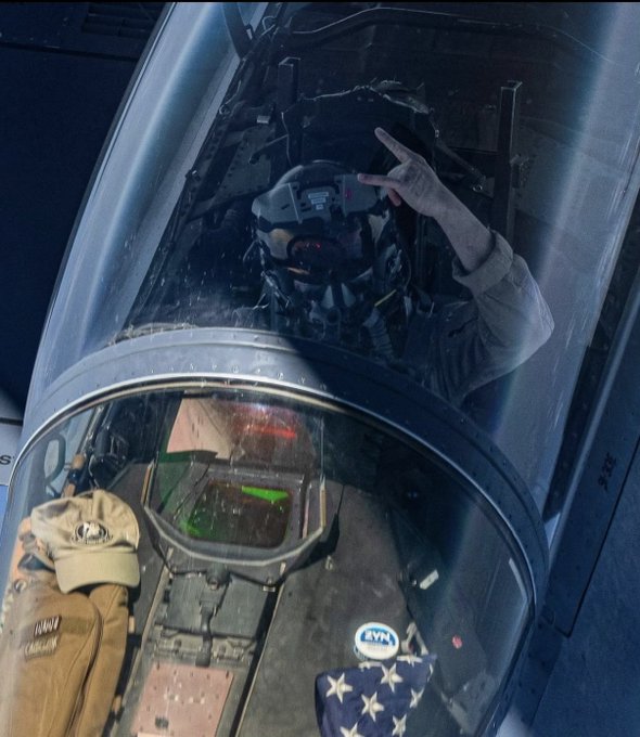 A pilot in a fighter jet cockpit flashes a peace sign, with a faded American flag and a "KVM" patch visible on the dashboard. The image fits the post perfectly—it captures an iconic, quintessentially American scene of military aviation pride.