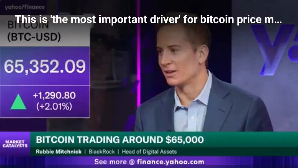 The image shows a man wearing a suit, standing in front of a computer screen displaying a news article about Bitcoin trading around $5,000. The man appears to be giving advice or discussing the current state of Bitcoin prices with someone on the other side of the screen.