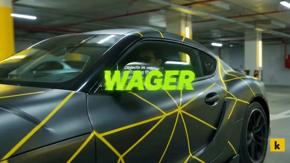 The image features a car with a unique design painted on its side, featuring yellow and black geometric patterns. The car's side has the word "WAGER" written on it in neon green letters. The car appears to be parked inside a garage or parking lot, as there are other cars visible in the background.