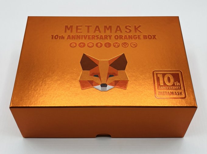An orange 'METAMASK 10th ANNIVERSARY ORANGE BOX' features a geometric fox logo and commemorates a decade of the crypto wallet.