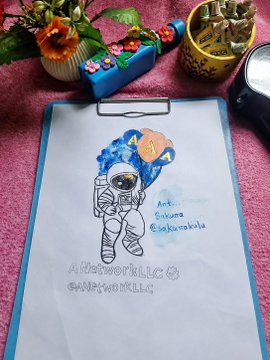 A child's drawing on a clipboard shows an astronaut with a blue background, signed 'Rati Sakuma @Sakumakids' with the text 'A New World In To #NEW WORLD'.