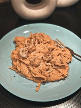 A teal plate holds a serving of creamy fettuccine pasta in a light sauce, with a fork resting on the side. The image humorously contrasts a simple, indulgent meal with the post's message about XRP earning passive income on Xora Finance rather than being spent on food.