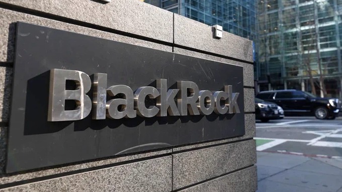 A metallic 'BlackRock' company sign mounted on a stone wall, with a modern glass building and black SUV visible in the background.