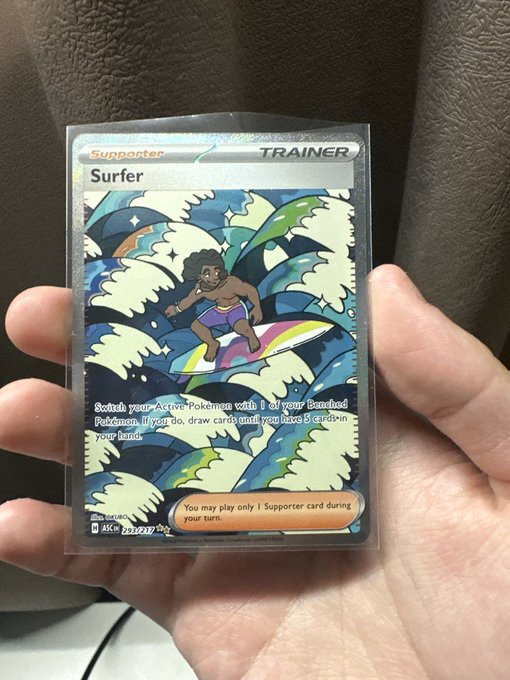 A hand holding a Pokémon TCG 'Surfer' Supporter Trainer card (ASC 263/264) depicting a surfer on a wave, with the ability text 'Switch your Active Pokémon with 1 of your Benched Pokémon.'