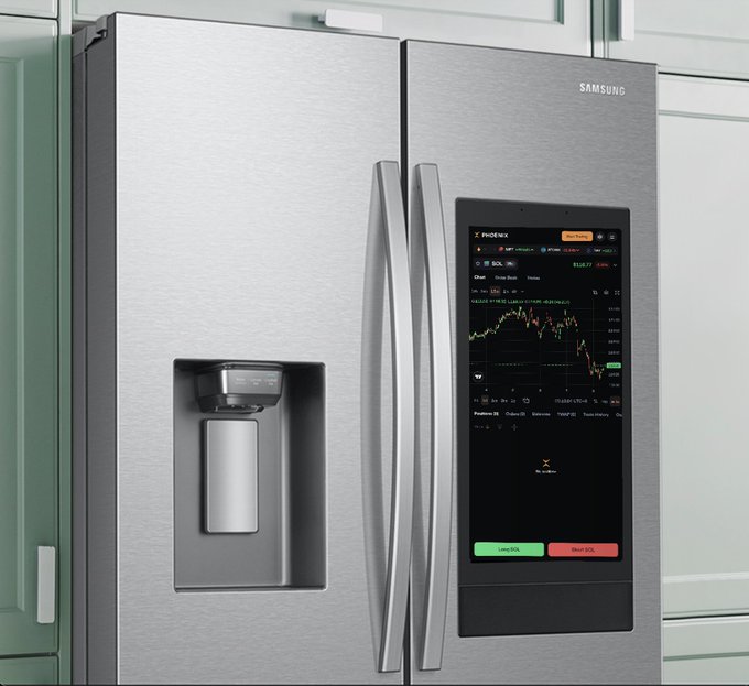 A Samsung stainless steel French door refrigerator with a water/ice dispenser on the left door and a large built-in touchscreen display on the right door showing a stock trading chart (appears to be SOL/Solana) and trading controls.