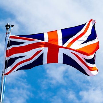 The image displays the Union Jack, the national flag of the United Kingdom, waving against a partly cloudy sky, symbolizing the UK's regulatory authority as the FCA prepares to enforce new crypto rules starting in late 2027.