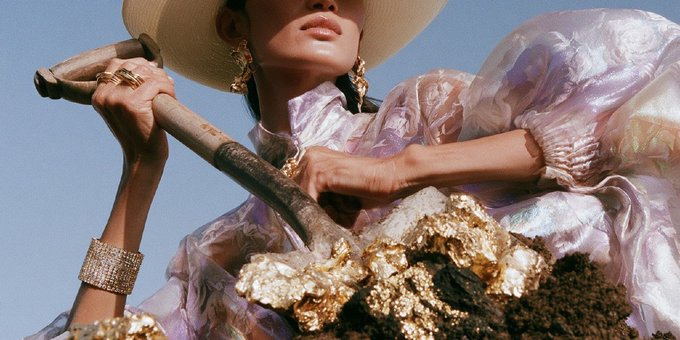 A woman in an opulent iridescent gown, wide-brimmed hat, and glittering jewelry holds a pickaxe over a chunk of gold ore, evoking the thrill of striking gold—a fitting visual metaphor for the post's hype around SOL and BTC, teasing an even bigger "gold rush" with the next token reveal.