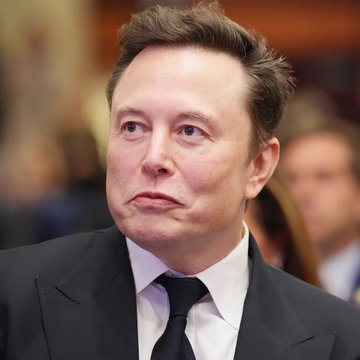 A close-up portrait of Elon Musk wearing a black suit and white shirt, looking off to the side with a serious expression.