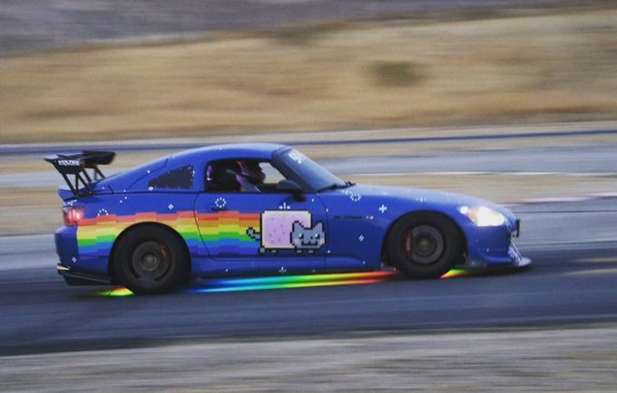 A blue sports car with a rainbow underglow and Nyan Cat pixel art decal races on a track with motion blur.