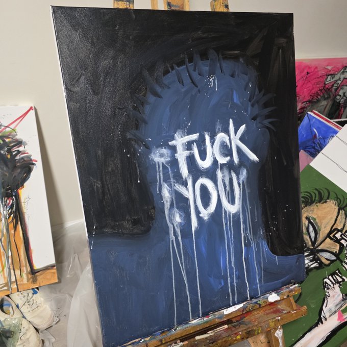 An expressive painting on a black background featuring the graffiti-style white text 'FUCK YOU' dripping down, with a blue silhouette resembling a spiky-haired head or hand behind it, displayed on an easel.