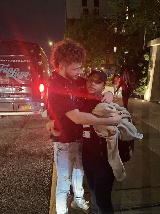 A nighttime photo of a man and woman hugging on a sidewalk next to a 'FunLuge' party van.
